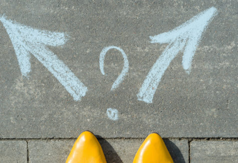 The tips of yellow pointed shoes in front of two chalk arrows pointing both left and right with a question mark between them.