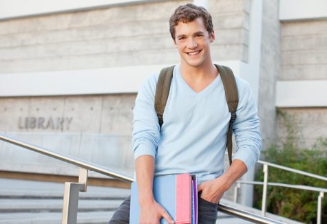 a high-school boy in a blue sweater standing outside his local library.