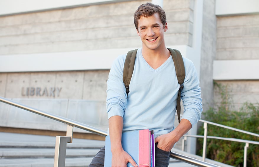 a high-school boy in a blue sweater standing outside his local library.