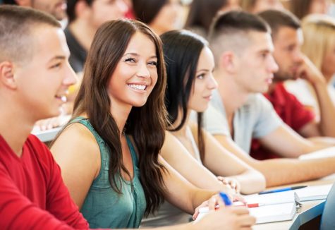 A female student smiling while in a lecture hall with many other students.