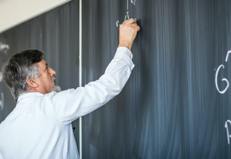 A teacher writing formulas on a chalk board.