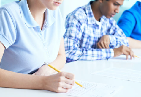 Several students taking tests on a long white table.