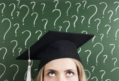 A graduating senior in her cap standing in front of a chalk board covered in question marks.