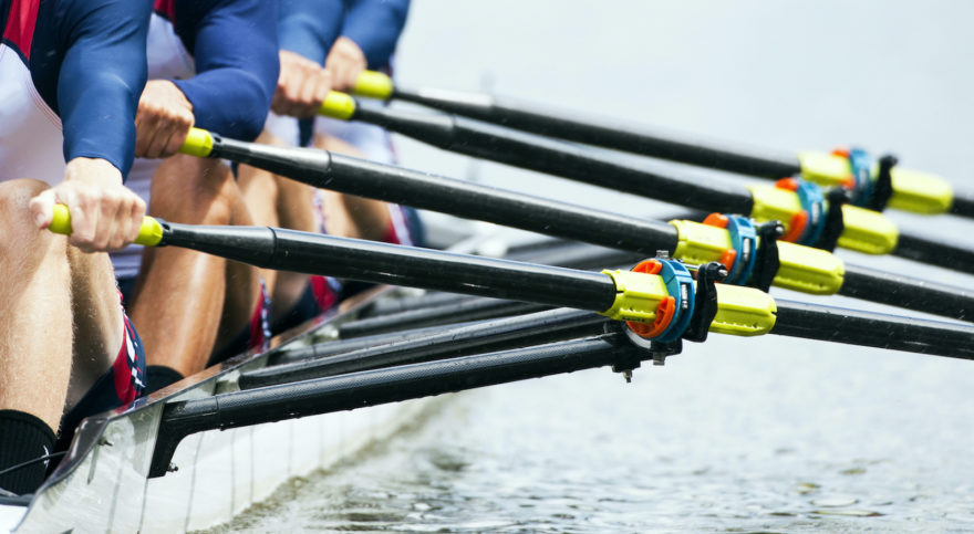 A Crew team practicing on a body of water with the focus on their oarlocks.