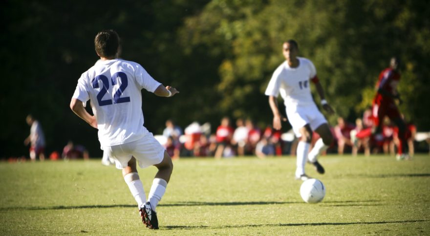 Two soccer teammates passing the ball in the middle of a soccer match.