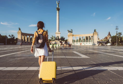 A female pulling her yellow rolling suitcase across a town square in a foreign city.