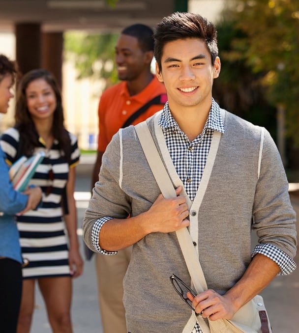 Smiling teenage boy of Asian descent standing outside school with classmates in background