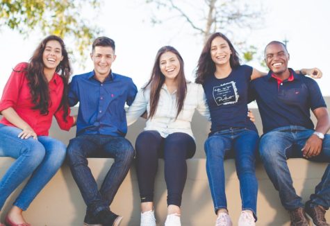 A set of five friends or roommates sitting together on a low wall.