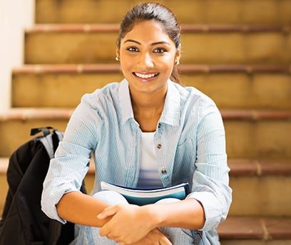 Smiling teen girl of Indian descent sitting on stairs inside school