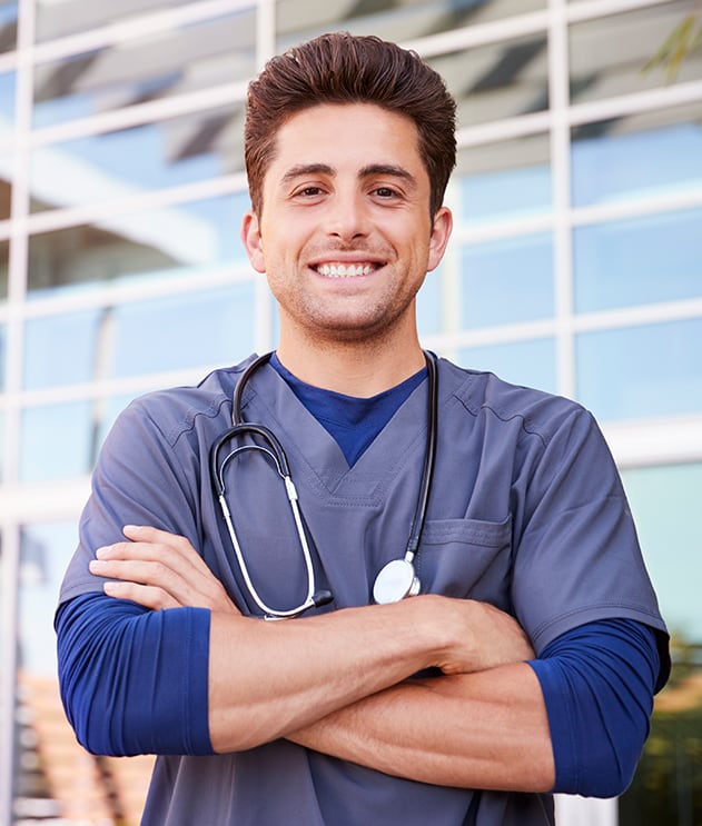 Smiling male med student in scrubs standing outside hospital