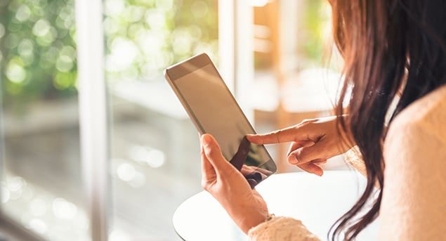 Close-up of woman with long brown hair holding an iPad and touching its screen